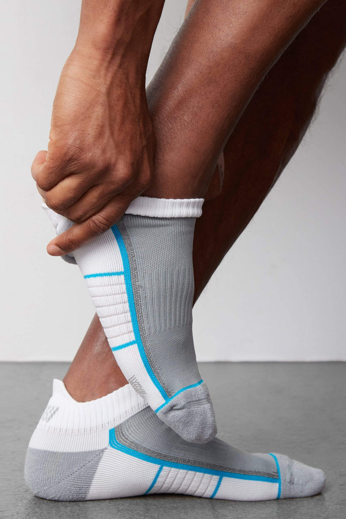 Side view of a man putting on AIRKNITx Ankle Sock in Bright White / Weldon Blue