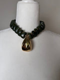 Olive green chunky bead necklace with a large polished gold drop pendant displayed on a jewelry bust.