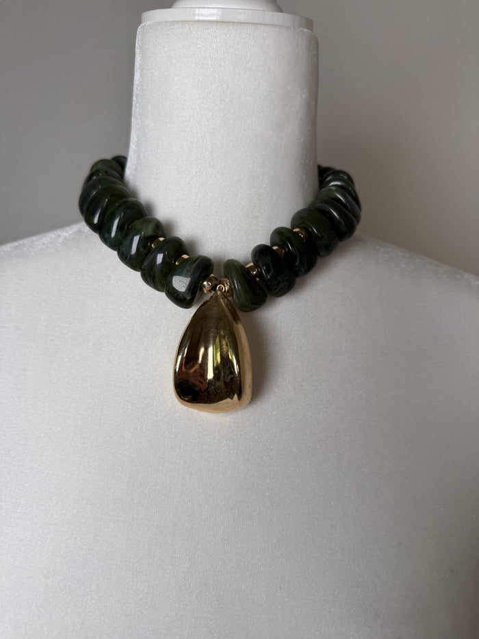 Olive green chunky bead necklace with a large polished gold drop pendant displayed on a jewelry bust.