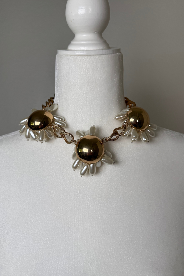 Golden Bloom statement necklace set with high-shine gold floral details, pearlized petal accents, a chunky chain, and matching earrings.
