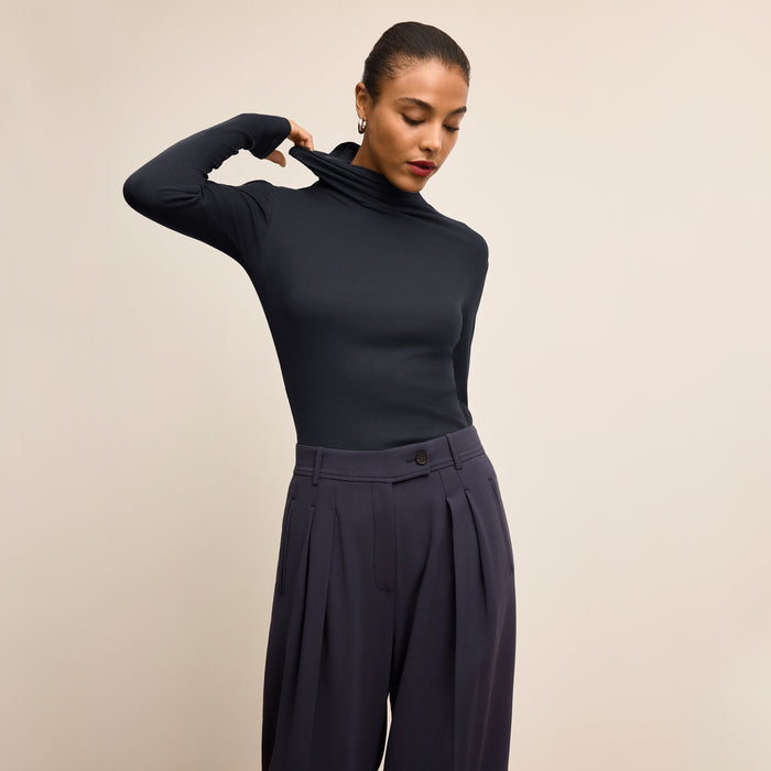 Woman wearing a navy turtleneck and pants against a beige background | Lead