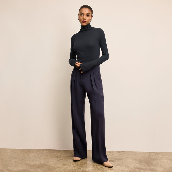 Woman wearing a navy turtleneck and pants against a beige background