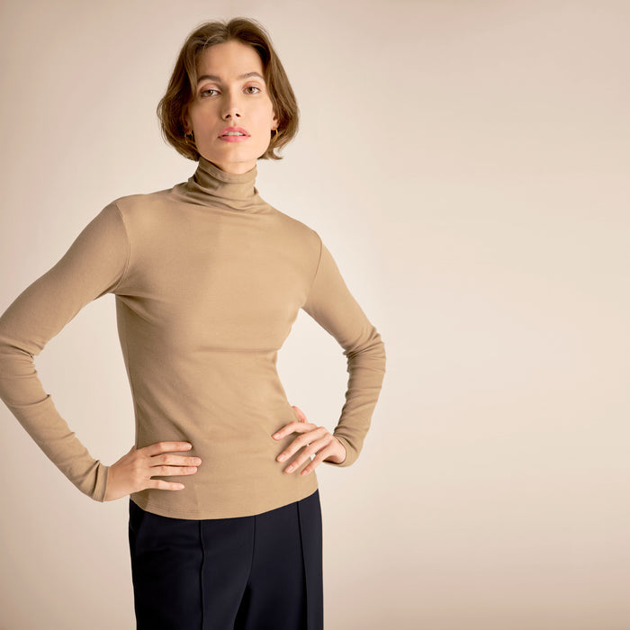 Woman wearing a beige turtleneck sweater against a beige background | Lead