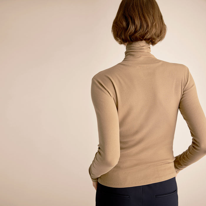 Woman wearing a beige turtleneck sweater against a beige background
