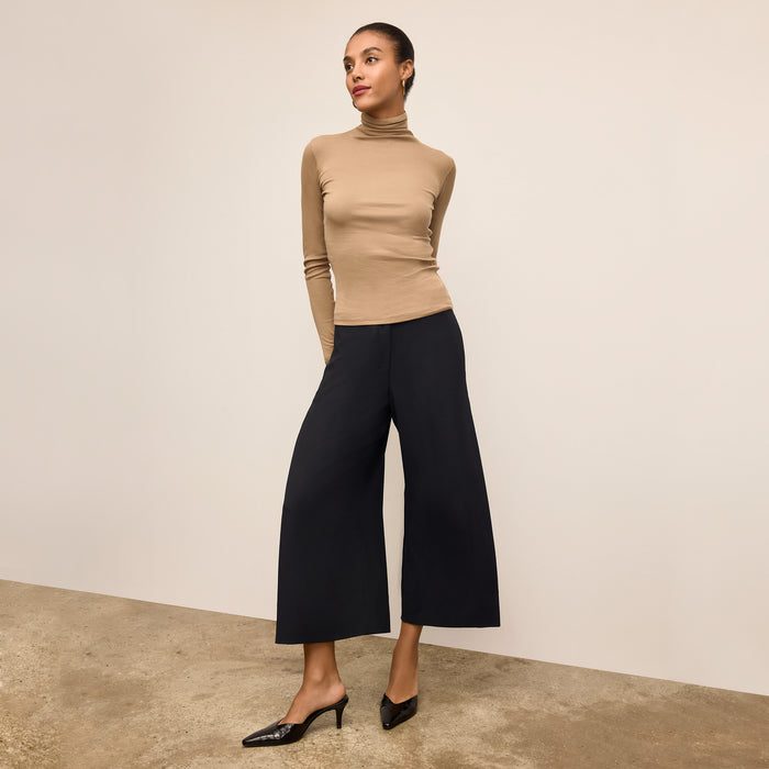 Woman wearing a beige turtleneck sweater against a beige background