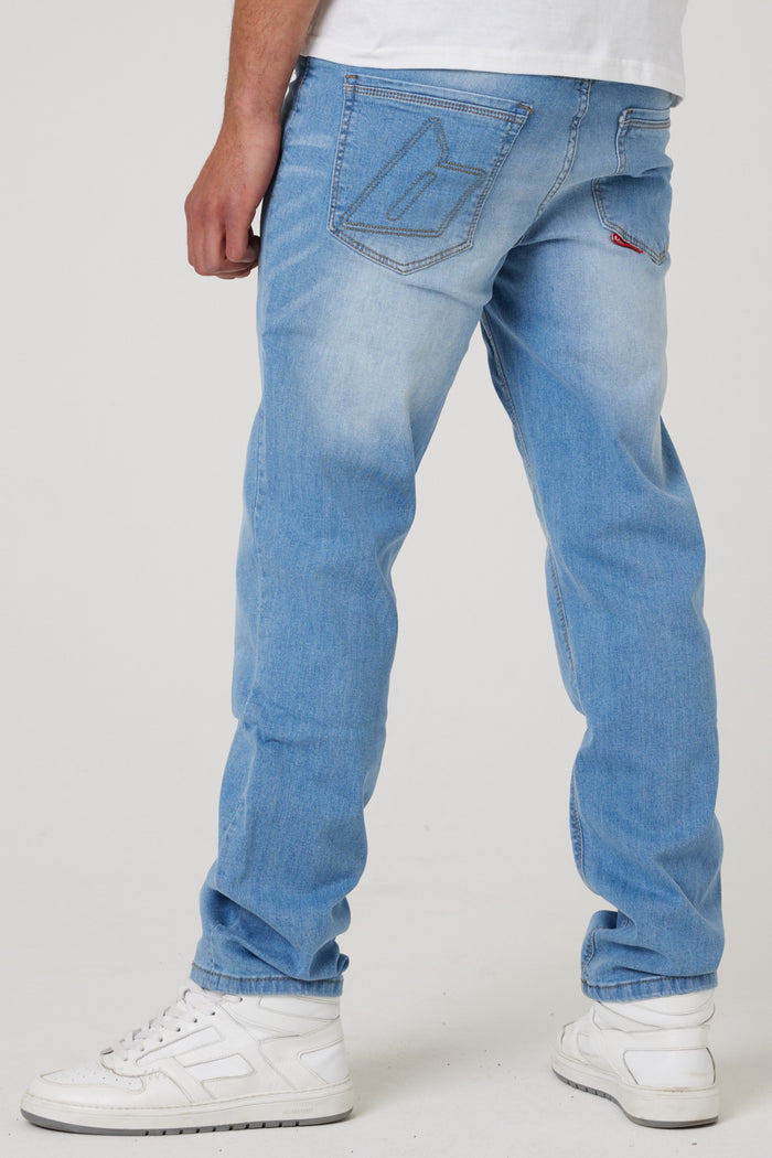 Someone wearing Beckenham Straight Fit Stretch Denim Jeans in Ice Blue with white sneakers stands with their back turned, one hand by their side. The straight leg jeans have a stitched design on the back pocket.