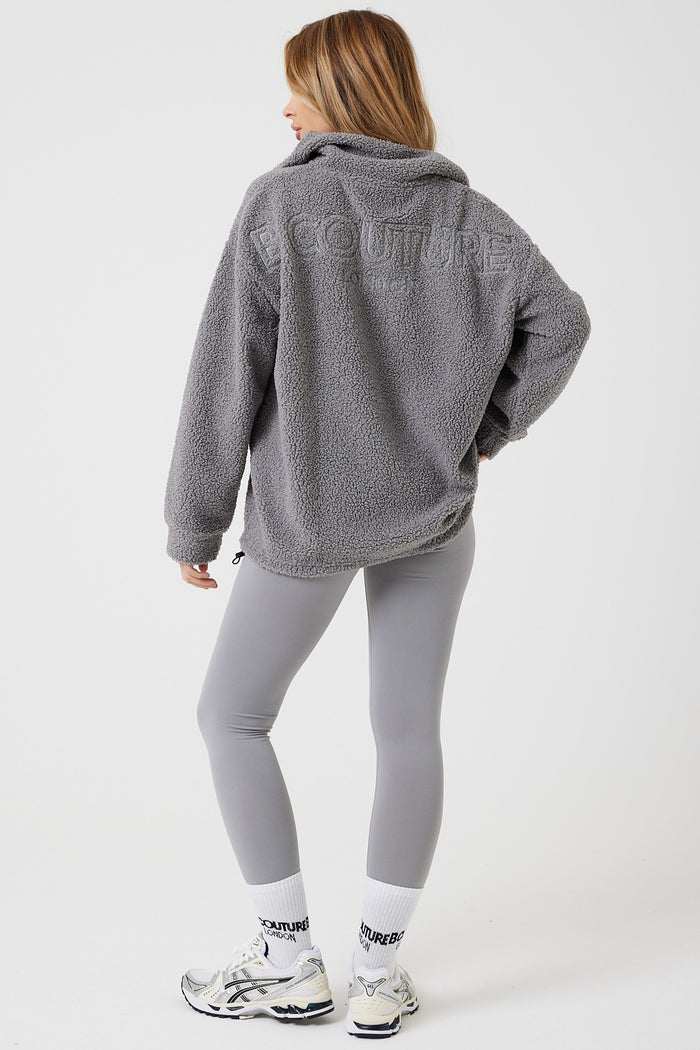 A woman stands facing away against a white background, wearing the Belmore Borg Jumper & Leggings Set in grey, featuring an embroidered back, paired with white socks and sneakers.