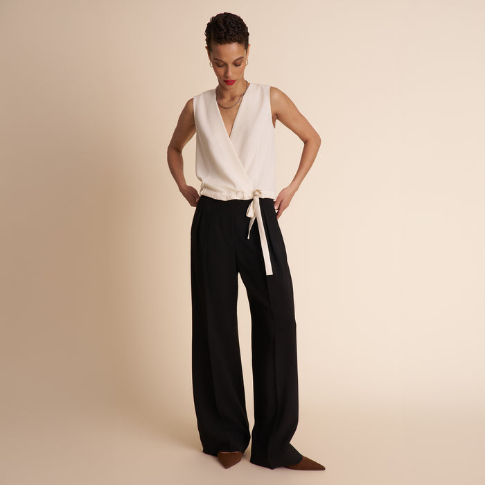 Woman wearing a white sleeveless top and black pants on a beige background