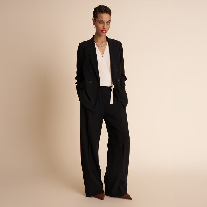 Woman wearing a black suit with a white shirt on a beige background
