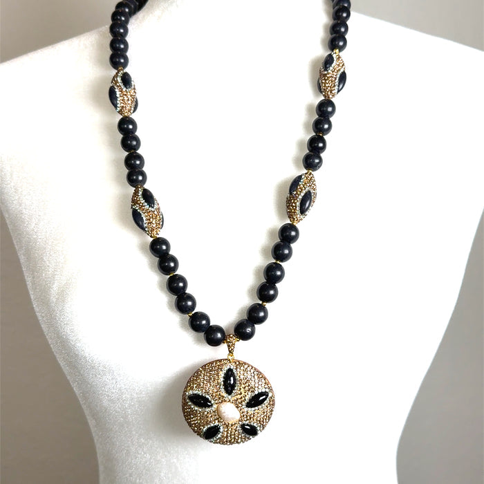 Long black gemstone and crystal beaded necklace with gold-tone detailing and an ornate round pendant.
