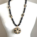 Long black gemstone and crystal beaded necklace with gold-tone detailing and an ornate round pendant.