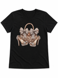 Black short sleeve graphic tee featuring a leopard print bag and heels design with sparkling bow accents on the front.