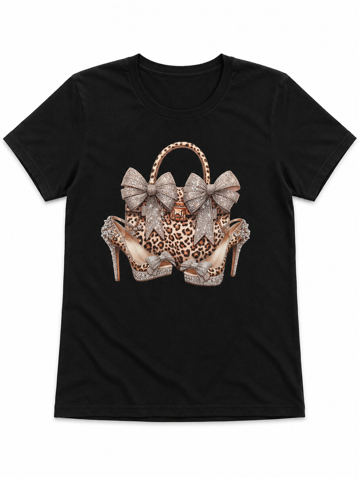 Black short sleeve graphic tee featuring a leopard print bag and heels design with sparkling bow accents on the front.