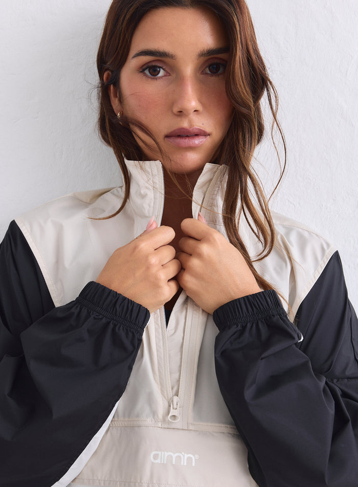 Lähikuva beigestä ja mustasta väriblokatusta aim'n windstopper-takista, jossa on puolivetoketjullinen kaulus [S-165cm]