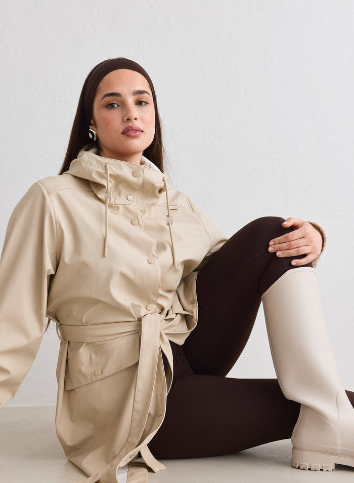 Nainen istumassa lattialla yllään aim'n Café Au Lait Rain Jacket [M-174cm]