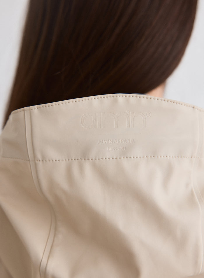 Lähikuva kohokuvioidusta aim'n-logosta Cafe Au Lait Rain Jacket -sadetakin selkäpuolella [M-174cm]