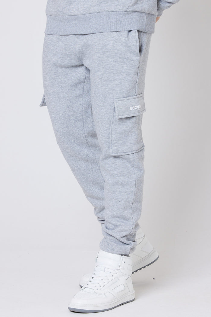 A male model wearing a pair of grey marl fleece cargo joggers with a regular fit, side pockets, and cuffed ankles. He is also wearing a dark-colored top and black sneakers.