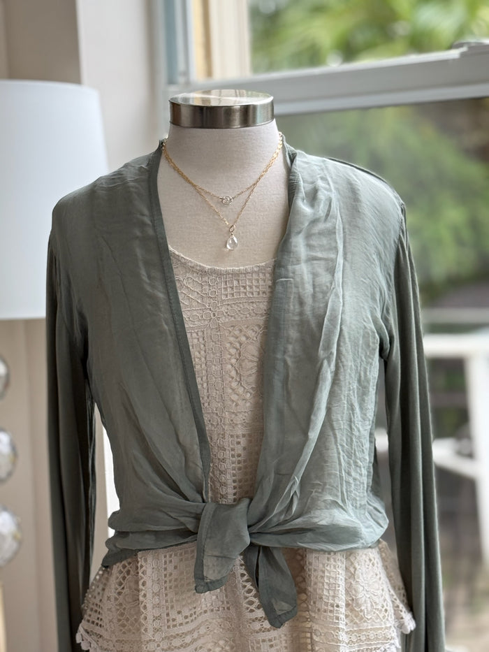 A green olive silk cardigan with a tie-front, displayed on a mannequin with  a necklace.