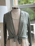 A green olive silk cardigan with a tie-front, displayed on a mannequin with  a necklace.