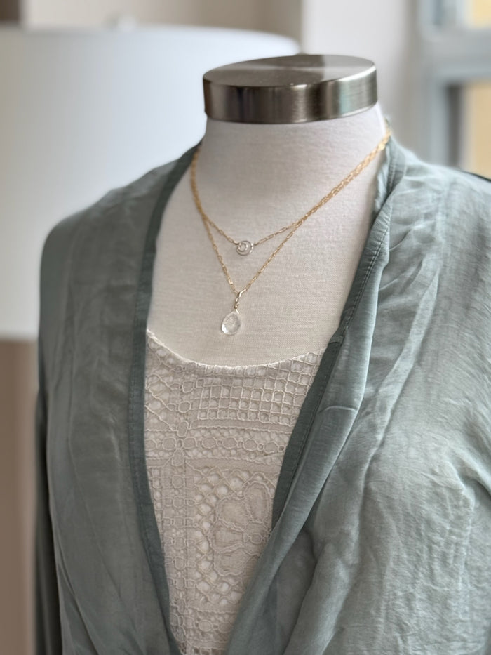 A green olive silk cardigan with a tie-front, displayed on a mannequin with  a necklace.
