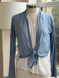 A blue silk cardigan with a V-neckline and long sleeves, displayed on a mannequin that is wearing a white top and has a necklace around its neck.