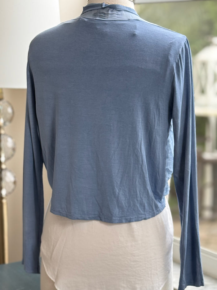 A blue silk cardigan with a V-neckline and long sleeves, displayed on a mannequin that is wearing a white top and has a necklace around its neck.
