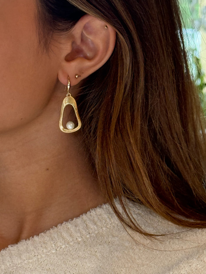 A pair of gold-tone hoop earrings with pearl accents on model
