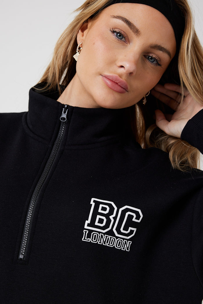 A person wearing the Collingwood Half-Zip Sweatshirt & Leggings Set in black, accessorized with a black headband and gold earrings, looks slightly upward while touching their hair.