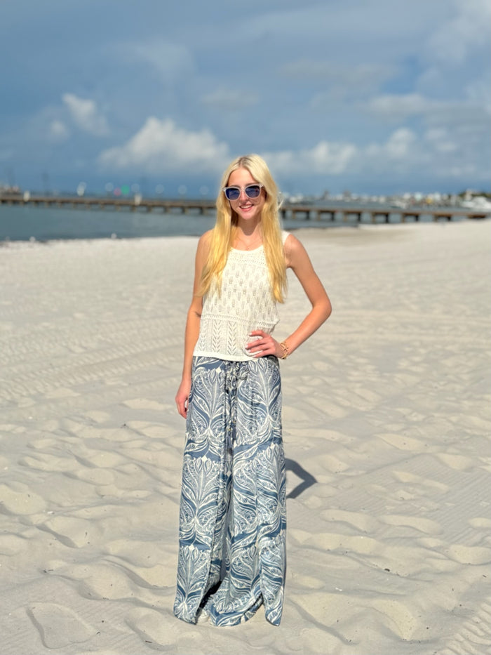 Woman with sunglasses standing on a sandy beach with a pier in the background