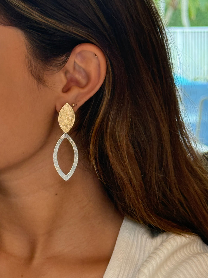 A pair of elongated hoop earrings with a hammered finish, featuring gold and silver colors.