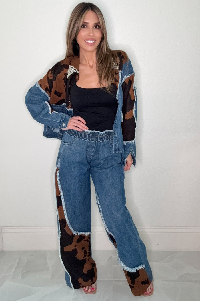 Blue straight leg jeans with faux suede cow print patch details, frayed trim, and an elastic waistband.