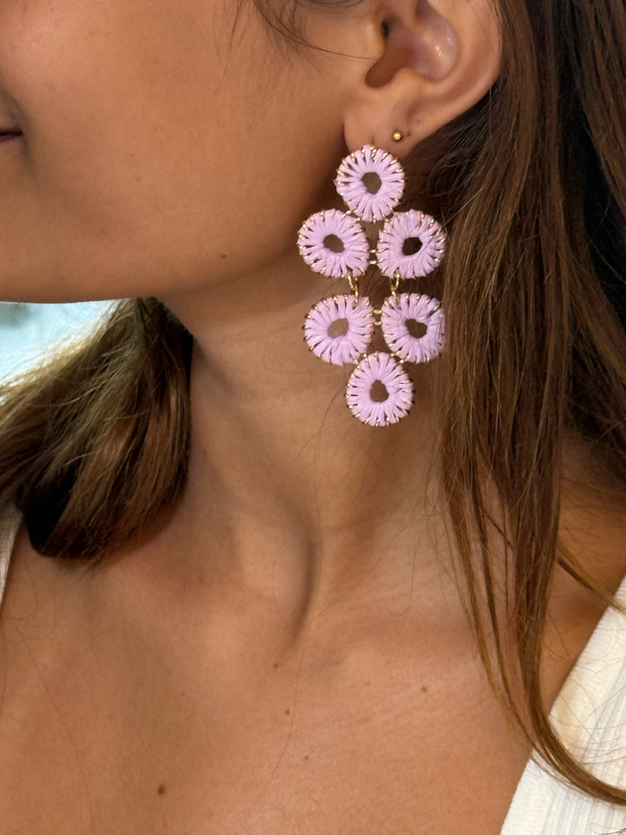 A close-up image of a woman wearing gold and purple floral earrings.