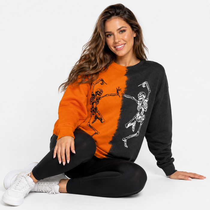 Woman wearing orange and black Halloween skeleton sweatshirt while seated in a clean white studio product setting.