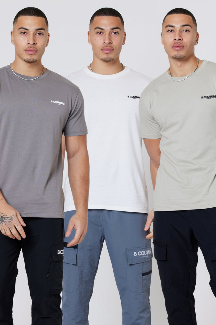 Three men in casual outfits pose together, each wearing a Hartfield 3-Pack Regular Cotton T-Shirt in Grey, Stone, or Cream. The classic tees and cargo pants stand out against the minimalist light background.