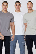 Three men in casual outfits pose together, each wearing a Hartfield 3-Pack Regular Cotton T-Shirt in Grey, Stone, or Cream. The classic tees and cargo pants stand out against the minimalist light background.