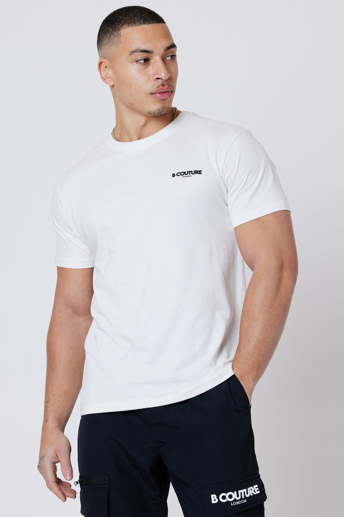 A man wearing a Hartfield 3-Pack Regular Cotton T-Shirt in cream and black shorts with signature branding poses against a plain light background, looking to his left with one hand by his side and the other in his pocket.