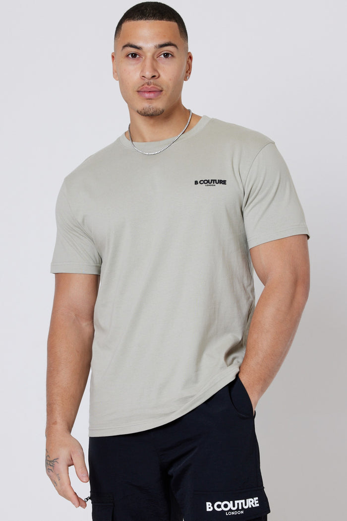 A man in a light grey Hartfield 3-Pack Regular Cotton T-Shirt and black branded shorts stands against a plain white background, looking at the camera with a neutral expression.