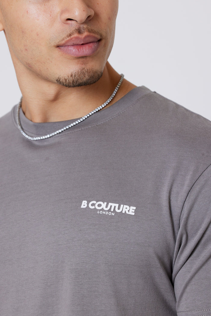 A person wearing the Hartfield 3-Pack Regular Cotton T-Shirt in grey with B Couture London signature white branding and a silver chain necklace, shown from the shoulders up with a partially visible face.