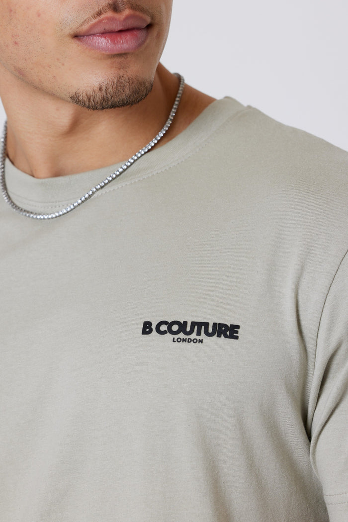 A person wears a cream crew neck from the Hartfield 3-Pack Regular Cotton T-Shirt (Grey/Stone/Cream), featuring “B Couture London” branding on the chest and a silver chain necklace; only their lower face and upper torso are visible.