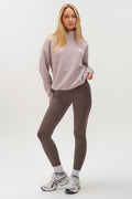 A woman with long blonde hair models the Hatherley Half-Zip Sweatshirt & Leggings Set in Stone, paired with white socks and sneakers. She stands confidently against a plain white background in this relaxed, cosy ensemble.