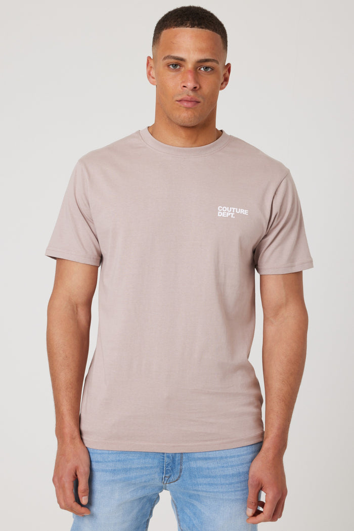 A man faces forward in a Haydon Walk Regular Fit Cotton T-Shirt - Beige with "COUTURE DEPT" in white on the left chest and light blue jeans, standing against a plain white background.