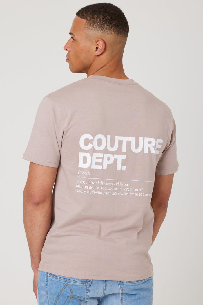 A man with short hair wears the beige Haydon Walk Regular Fit Cotton T-Shirt, crafted from a soft blend. "COUTURE DEPT." and a definition in white text appear on the back. He faces away, pairing it with light blue jeans for a classic look.