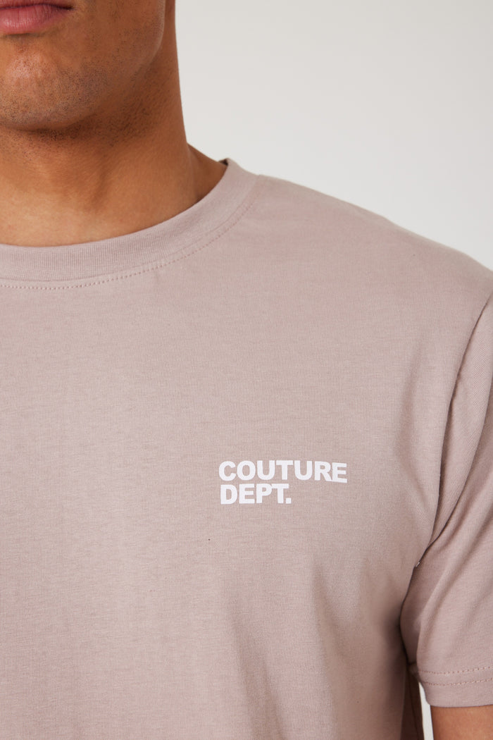 A person wears the Haydon Walk Regular Fit Cotton T-Shirt in beige, crafted from a soft cotton blend with "COUTURE DEPT." in white on the left chest. Only the lower face and upper torso are visible—an essential wardrobe staple.