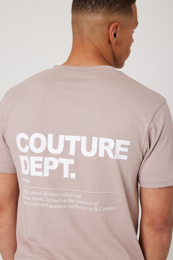 A man faces away, wearing the Haydon Walk Regular Fit Cotton T-Shirt in beige, featuring bold white "COUTURE DEPT." text and a smaller definition below; the shirt’s striking text is the main highlight.
