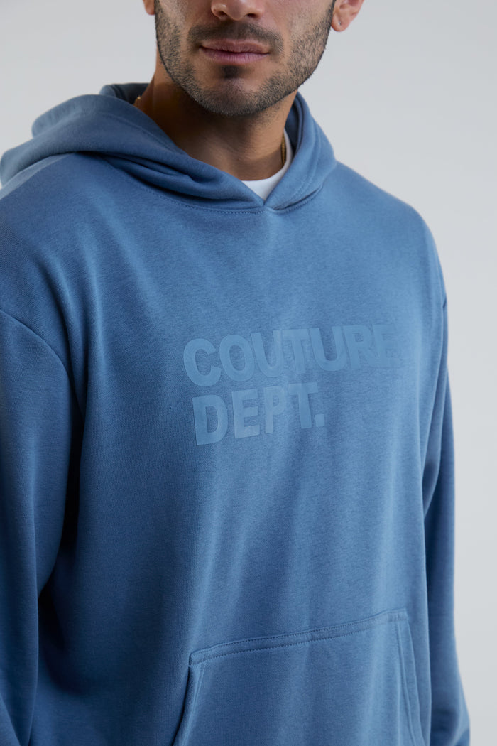 Person wearing a blue hoodie with 'Couture Dept.' text on a plain background