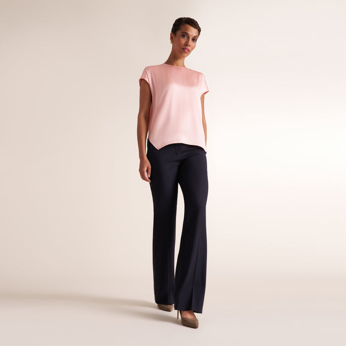 A woman modeling a light pink short-sleeve top and dark navy wide-leg trousers against a plain light beige studio background.