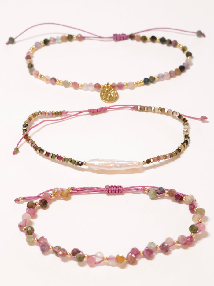 Set of three beaded bracelets with pink strings on a white background