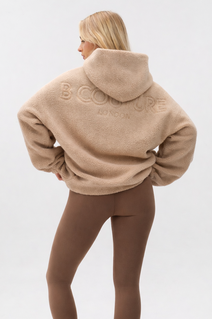 A person with long blonde hair models the Isla Sherpa Hoodie & Leggings Set in Beige/Brown, featuring cozy fleece and brown leggings, standing against a plain light background with their back to the camera.