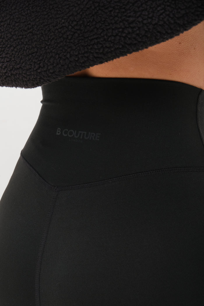 Close-up of a person wearing the Isla Sherpa Hoodie & Leggings Set - Black, featuring high-waisted leggings with B COUTURE LONDON logo and a cosy black sherpa hoodie for added warmth.