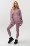 A woman with long blonde hair poses confidently against a white background in the Isla Sherpa Hoodie & Leggings Set - Mauve, paired with black ankle boots and white socks.
